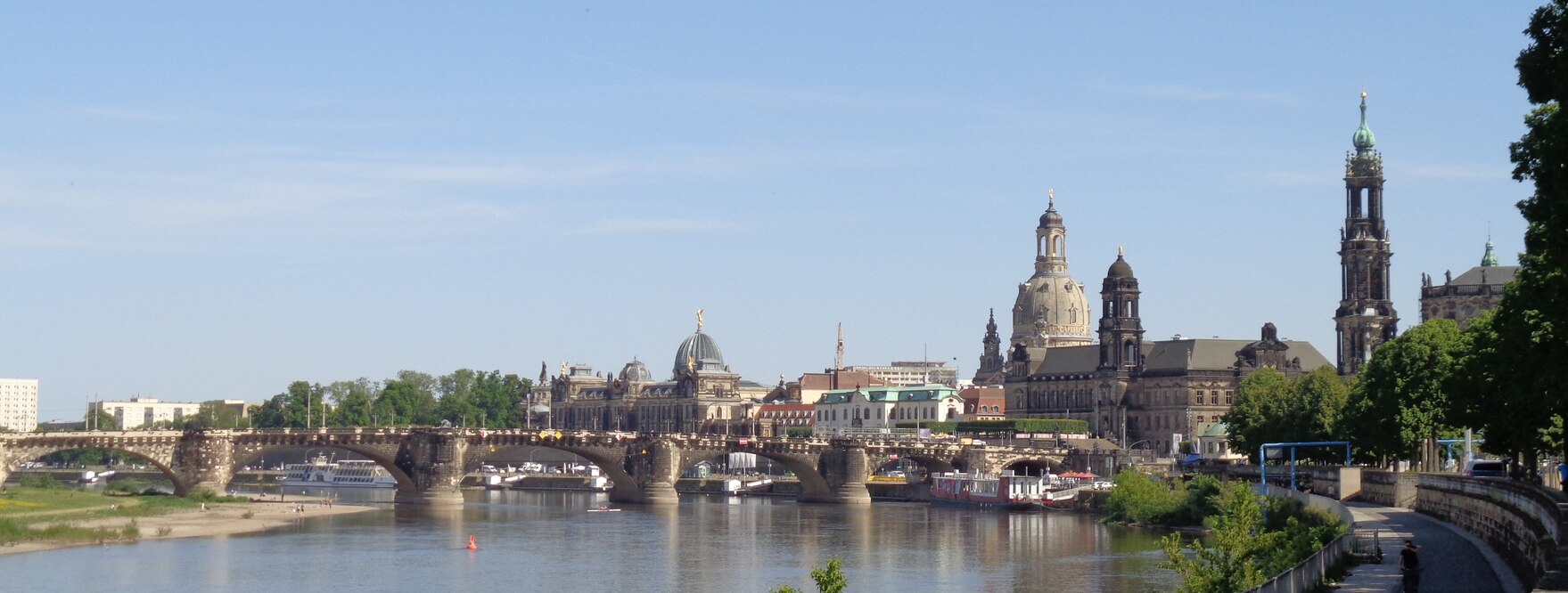 Blick auf Dresdens Altstadt über die Elbe von Westen, mit Augustusbrücke, Frauenkirche, Turm der katholischen Hofkirche, Schiffsanlegestellen unter der Brücke, blauer Himmel mit Schleierwolken